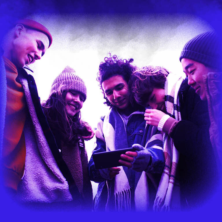 Das Bild zeigt eine Gruppe junger Leute, welche in Winterkleidung auf ein Handy schauen.